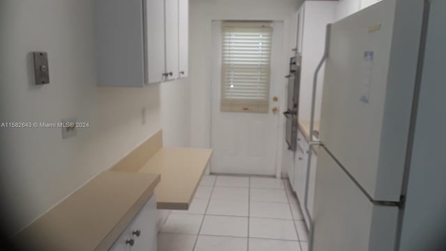 kitchen with white refrigerator, white cabinets, and light tile floors