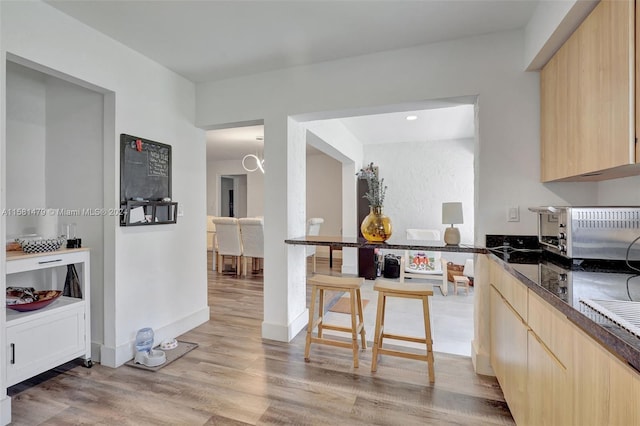 kitchen featuring light hardwood / wood-style flooring, dark stone countertops, and light brown cabinets