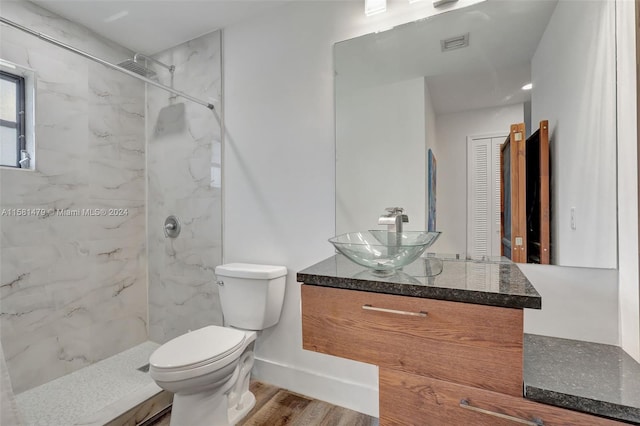 bathroom featuring wood-type flooring, vanity, toilet, and a tile shower