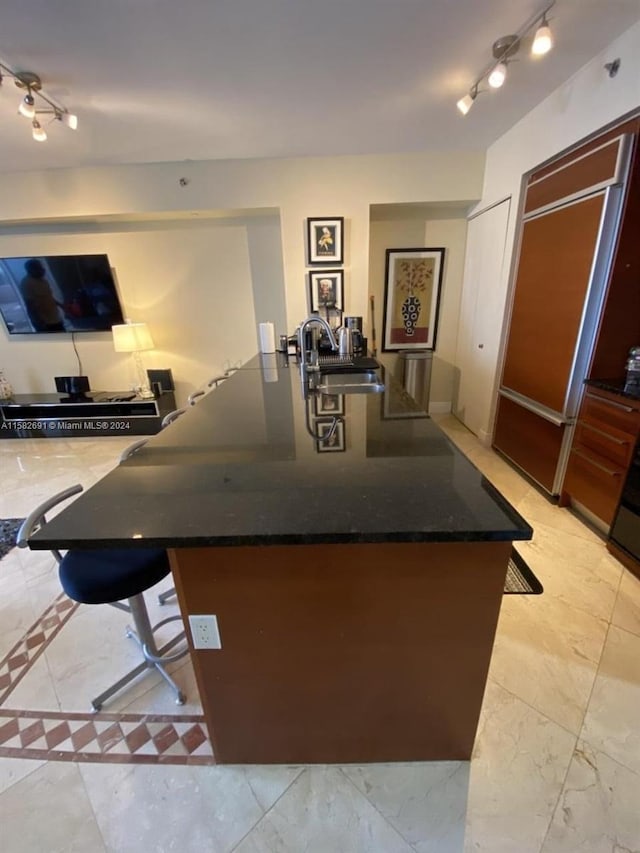 kitchen with dark stone countertops, rail lighting, sink, and light tile floors