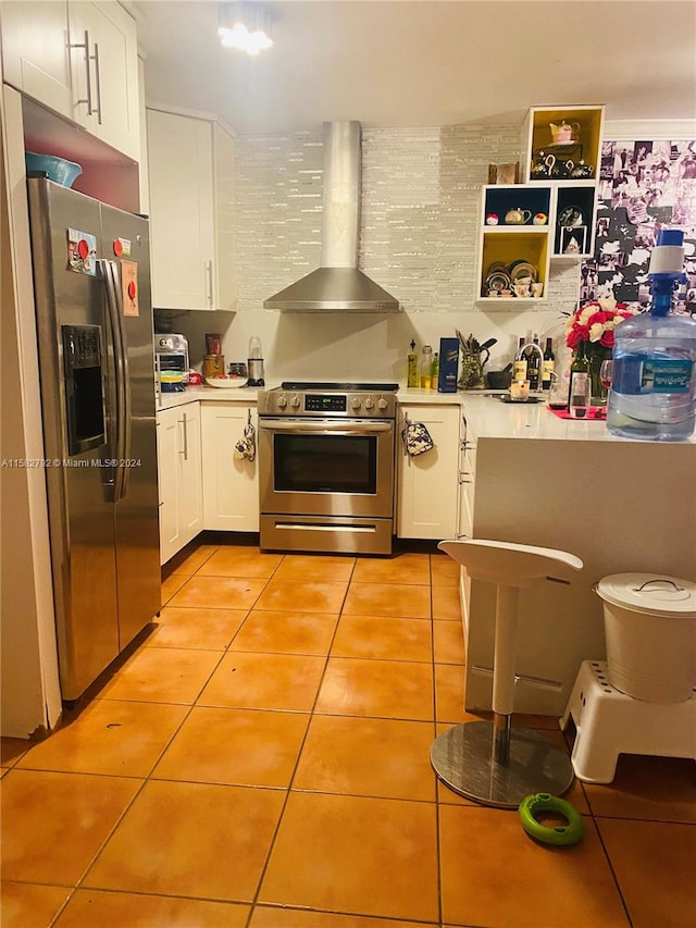 kitchen featuring white cabinetry, stainless steel appliances, light tile patterned floors, and wall chimney range hood