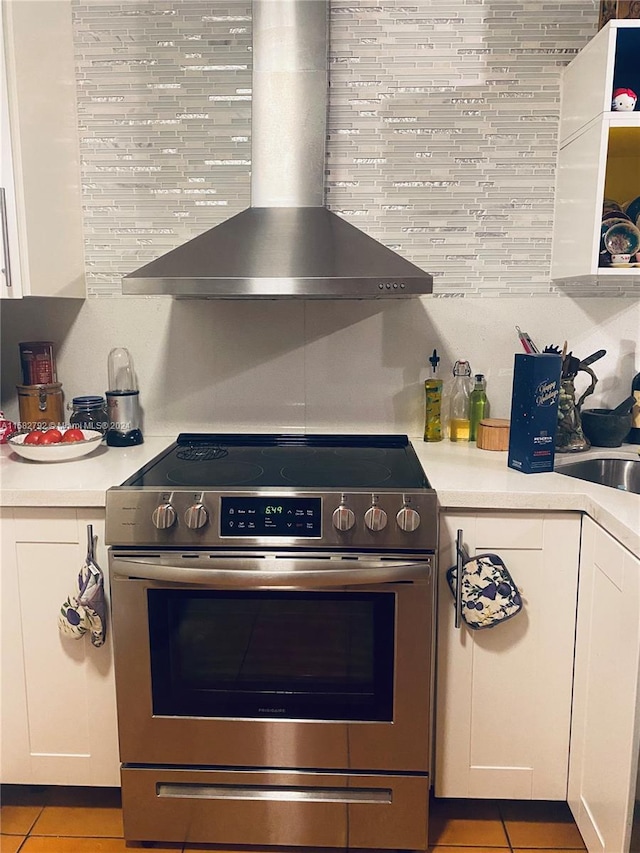 kitchen with stainless steel range, wall chimney exhaust hood, light tile patterned flooring, and white cabinets