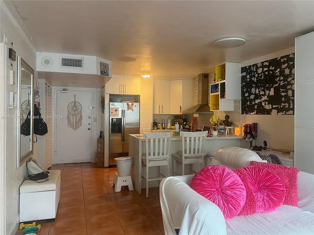 kitchen featuring wall chimney range hood, white cabinetry, tile patterned flooring, and stainless steel fridge with ice dispenser