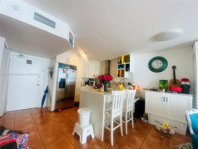 kitchen featuring white cabinets, stainless steel fridge with ice dispenser, tile patterned flooring, and kitchen peninsula