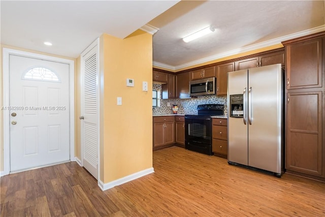 kitchen with crown molding, appliances with stainless steel finishes, backsplash, and light wood-type flooring