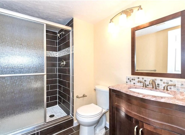 bathroom featuring vanity, toilet, a shower with shower door, and backsplash