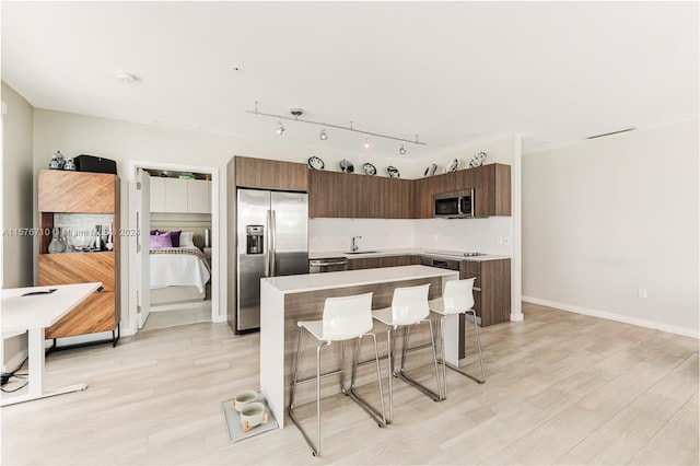 kitchen with a kitchen breakfast bar, stainless steel appliances, sink, light hardwood / wood-style flooring, and a center island