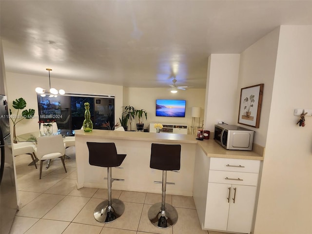 kitchen with white cabinets, ceiling fan with notable chandelier, light tile floors, and a kitchen bar