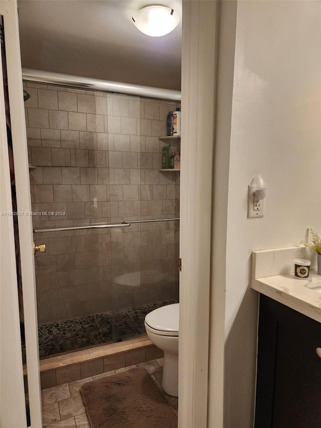 bathroom featuring a shower with door, toilet, tile floors, and vanity