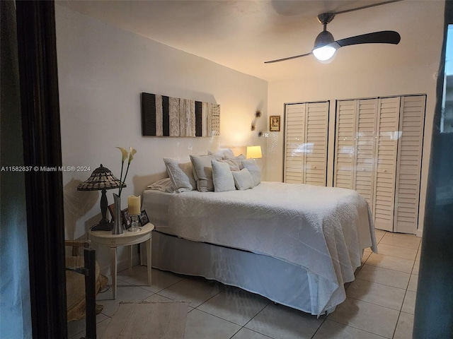 tiled bedroom with ceiling fan and two closets