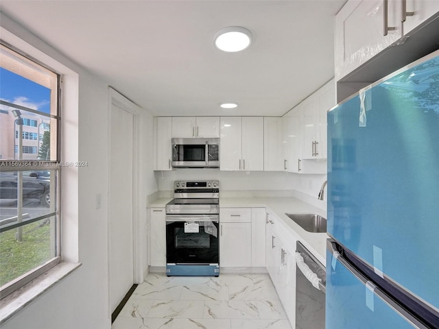 kitchen with appliances with stainless steel finishes, white cabinets, light tile patterned floors, and sink