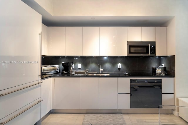 kitchen with tasteful backsplash, oven, white cabinets, sink, and light tile floors