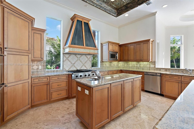 kitchen featuring stainless steel appliances, crown molding, light tile flooring, a center island with sink, and tasteful backsplash