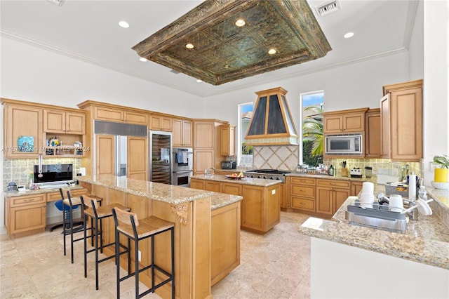 kitchen featuring a center island, built in appliances, custom exhaust hood, light tile floors, and tasteful backsplash