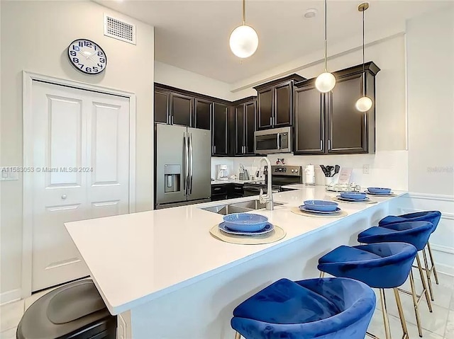 kitchen with a breakfast bar, kitchen peninsula, appliances with stainless steel finishes, light tile floors, and dark brown cabinetry