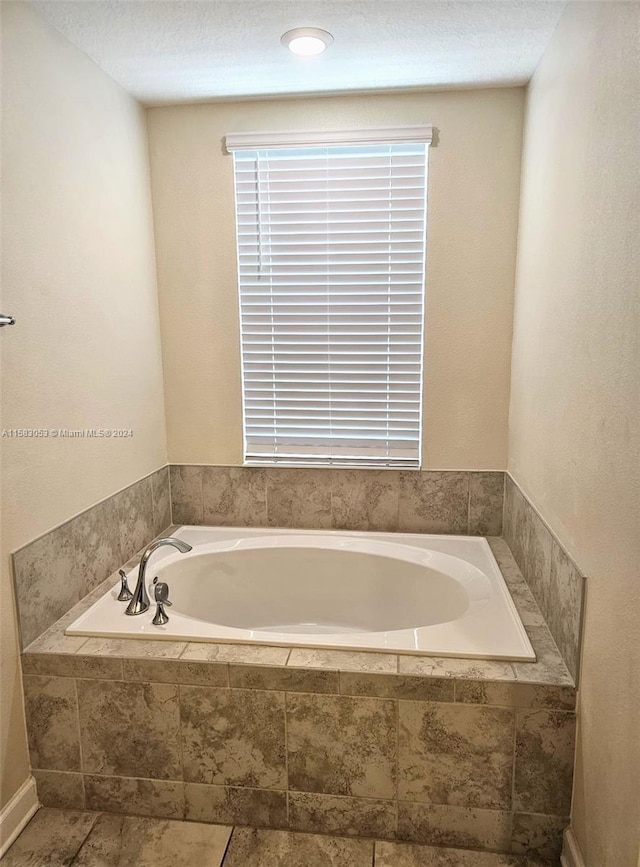 bathroom with tile flooring, tiled tub, and a textured ceiling