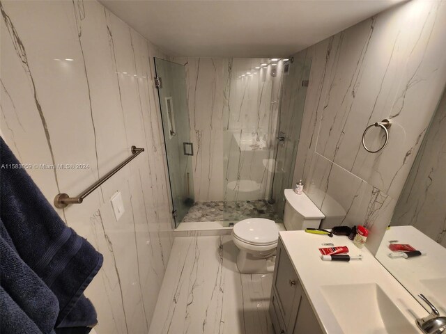 bathroom with a shower with door, vanity, tile patterned flooring, tile walls, and toilet