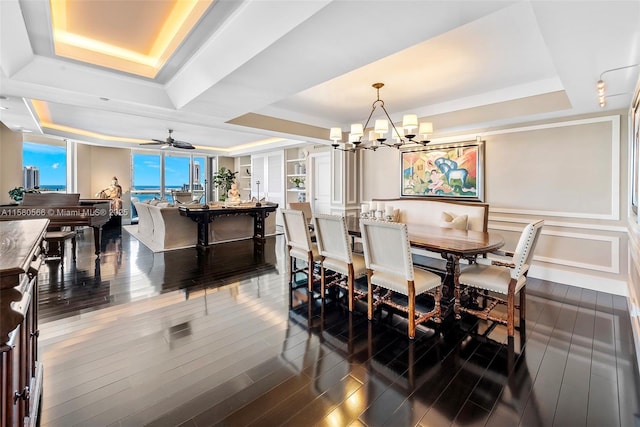 dining area with a raised ceiling, ceiling fan with notable chandelier, and dark hardwood / wood-style flooring