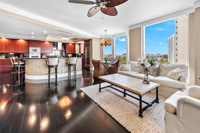 living room with dark wood-style floors, recessed lighting, a city view, and ceiling fan with notable chandelier