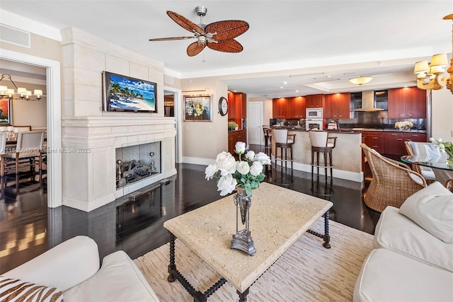 living area featuring recessed lighting, dark wood-type flooring, a large fireplace, baseboards, and ceiling fan with notable chandelier