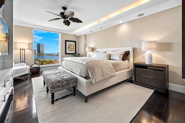 bedroom with baseboards, dark wood-style floors, ceiling fan, a water view, and a city view