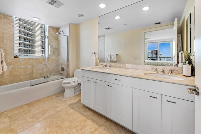 full bathroom featuring toilet, a sink, visible vents, combined bath / shower with glass door, and double vanity