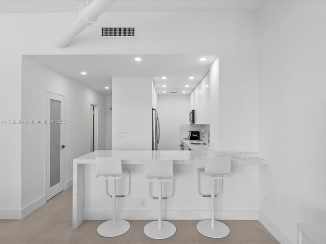 kitchen featuring kitchen peninsula, white cabinets, a kitchen breakfast bar, and sink