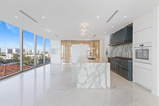 kitchen featuring white cabinets, oven, a large island, wall chimney range hood, and floor to ceiling windows