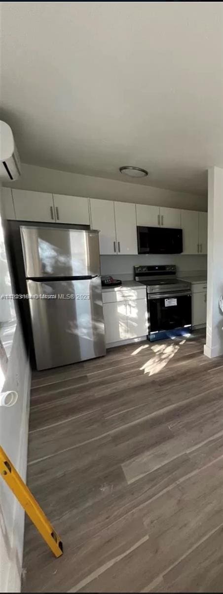 kitchen with stainless steel refrigerator, white cabinetry, dark hardwood / wood-style floors, an AC wall unit, and electric stove