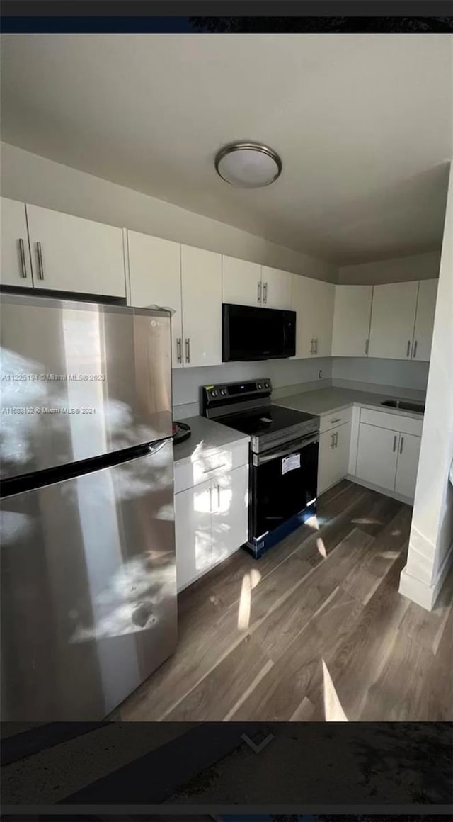 kitchen with white cabinetry, sink, black appliances, and hardwood / wood-style floors