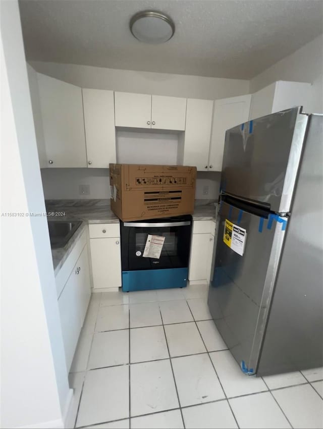 kitchen with white cabinets, sink, light tile flooring, and stainless steel fridge