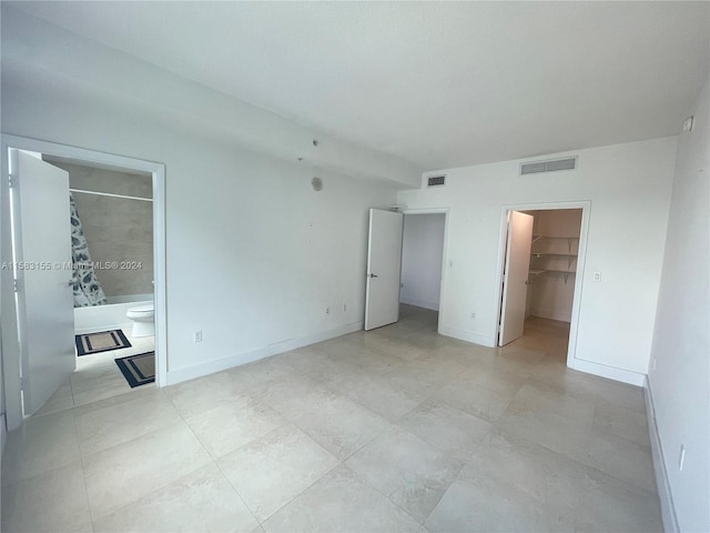 unfurnished bedroom featuring ensuite bath, a spacious closet, a closet, and light tile flooring