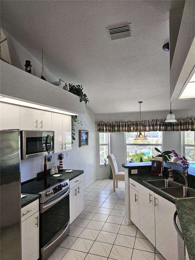 kitchen with pendant lighting, sink, appliances with stainless steel finishes, white cabinetry, and a textured ceiling