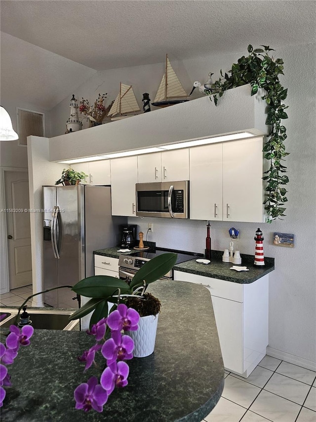 kitchen featuring lofted ceiling, white cabinetry, a textured ceiling, light tile patterned floors, and appliances with stainless steel finishes