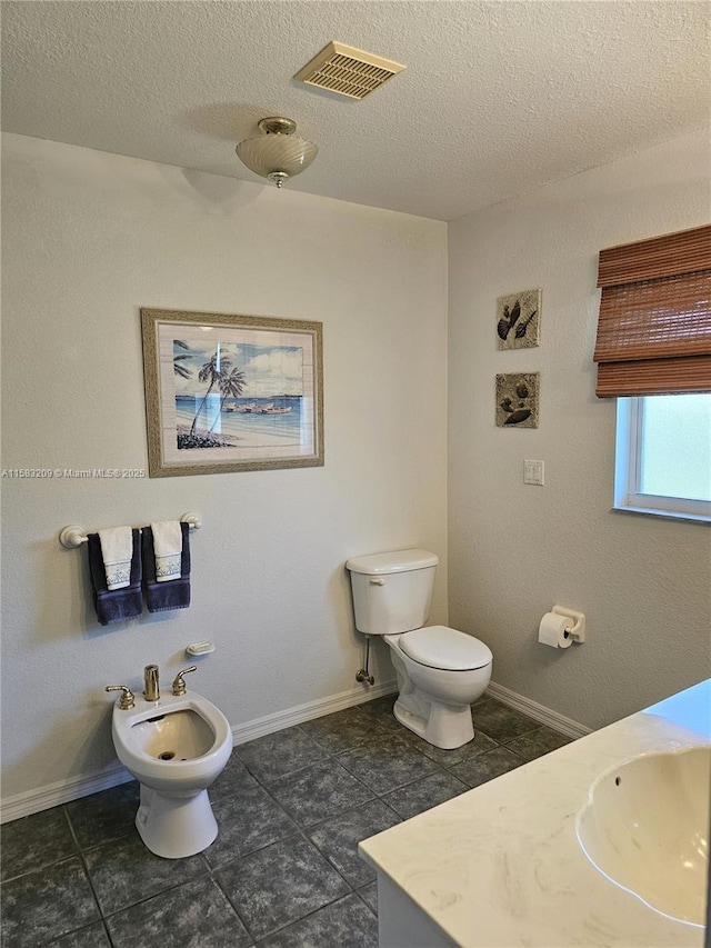 bathroom featuring a bidet, vanity, toilet, and a textured ceiling