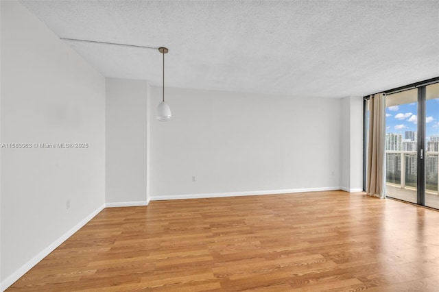 spare room featuring a wall of windows, a textured ceiling, and light hardwood / wood-style flooring