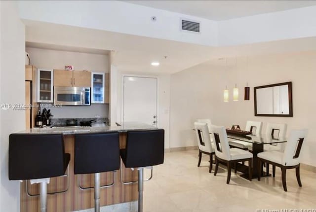 kitchen with kitchen peninsula, light brown cabinets, light tile floors, and a breakfast bar area