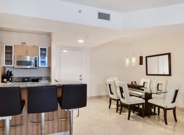 kitchen with light stone counters, light tile floors, a kitchen bar, hanging light fixtures, and kitchen peninsula