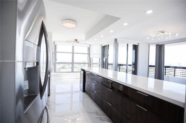 kitchen with stainless steel refrigerator, a tray ceiling, dark brown cabinets, light tile floors, and track lighting