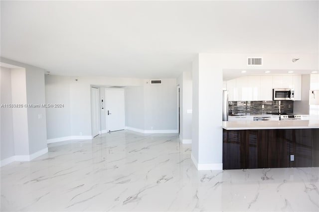 kitchen with appliances with stainless steel finishes, backsplash, light tile floors, and white cabinetry