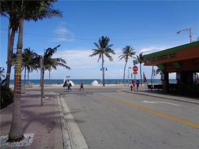 view of street with street lights, curbs, a water view, and sidewalks