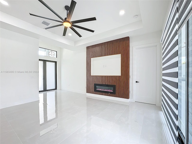 unfurnished living room featuring french doors, ceiling fan, light tile flooring, and a raised ceiling