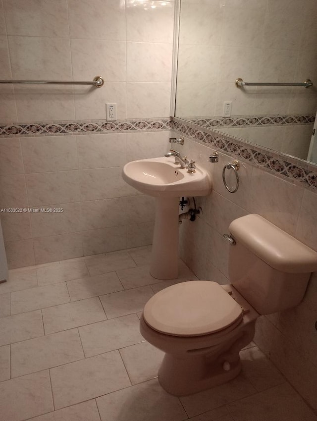 bathroom featuring tile patterned floors, toilet, sink, and tile walls