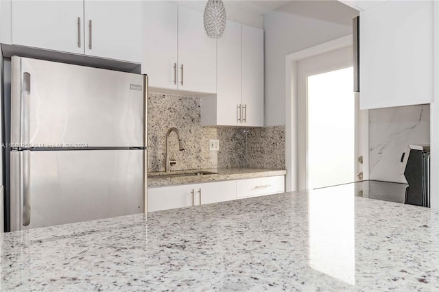 kitchen with stainless steel refrigerator, white cabinetry, light stone countertops, and decorative backsplash