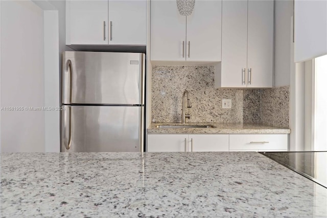 kitchen with tasteful backsplash, light stone counters, sink, white cabinetry, and stainless steel refrigerator