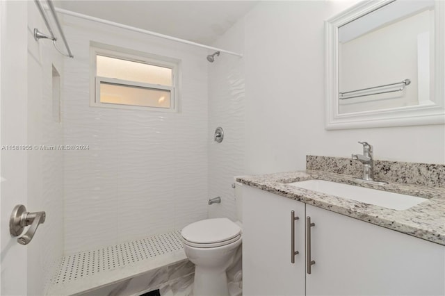 bathroom with a tile shower, vanity, and toilet