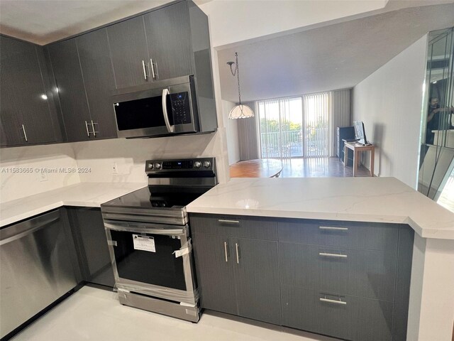 kitchen with appliances with stainless steel finishes, light stone countertops, backsplash, and hanging light fixtures