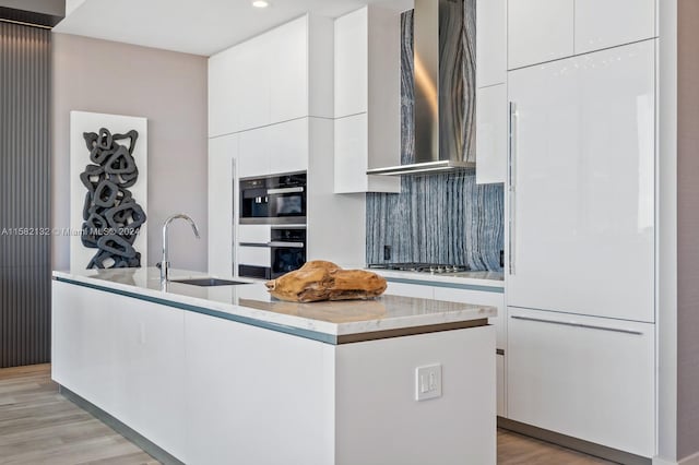 kitchen with white cabinets, wall chimney range hood, sink, light hardwood / wood-style floors, and stainless steel appliances