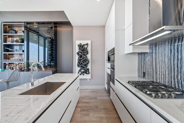 kitchen with appliances with stainless steel finishes, white cabinetry, wall chimney exhaust hood, and sink