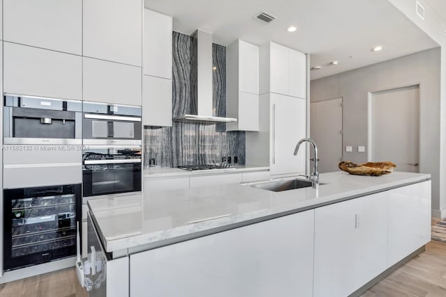 kitchen with light stone countertops, wall chimney exhaust hood, beverage cooler, sink, and light hardwood / wood-style floors